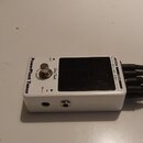 Bílý kytarový pedál s nápisem PowerPlant Tuner a logem Harley Benton. Zařízení má stříbrný spínač s nápisem True Bypass, displej a konektory IN a OUT…