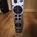 Zadní strana stříbrného rackového zesilovače. Na horní části je nápis behringer MODEL NU4-6000 a CIRCUIT BREAKER. Zařízení má dva chladicí ventilátor…