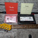 Fotografie zachycuje kráček elektrické kytary s nápisy Fender a TELECASTER, hmatník z tmavého dřeva a doprovodné dokumenty. V horní části je červený…