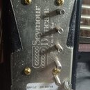 Zadní strana kovového snímače v černém plastovém rámu. Na kovovém krytu je vyryto logo a nápis Seymour Duncan. V dolní části je bílá nálepka s texty…
