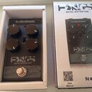Fotografie zobrazuje efekt pedál v bílém originálním pudele a vedle něj jeho krabici. Pedál je černé barvy s nápisy tc electronic a FANGS METAL DISTO…