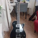 Černá elektrická kytara s dvojcutem a bílým bindingem. Na hlavě je nápis GRETSCH. Nástroj má dva snímače, stříbrný Bigsby vibrato systém a čtyři ovlá…