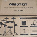 Fotografie zobrazuje dvě kartonové krabice s elektronickou bicí sadou. Na horní krabici je nápis DEBUT KIT, Mesh-Head Electronic Drum Kit Bundle a PO…