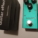 Zelený efekt pedál s nápisem Analog Delay a TRUE BYPASS. Na horní straně jsou tři černé ovládací knoflíky s popisky Time, Mix a Repeat. Vedle pedálu…