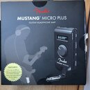 Fotografie znázorňuje originální černé balení sluchátkového zesilovače s nápisy Fender, MUSTANG™ MICRO PLUS a GUITAR HEADPHONE AMP. Na krabici je zob…