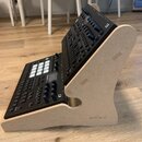 Dva černé elektronické hudební kontroléry umístěné v dřevěném stojanu z MDF desky. Na levém zařízení je čitelný nápis Ableton Push a logo Novation. N…