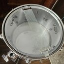 Fotografie zachycuje snare drum z ptačí perspektivy. Na bílém koženu jsou vidět nápisy MAPEX a UX REMO DRUM HEAD MADE BY REMO IN USA. Přes buben je n…