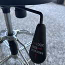 Detailní záběr na černou plastovou páčku pro regulaci výšky sedátka. Na povrchu páčky je bílý nápis LOCK se šipkou vlevo, FREE se šipkou vpravo a UP…