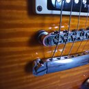 Detail elektrické kytary s žlutohnatým plamenovitým povrchem. Je vidět část snímače v bílém rámečku s neúplným nápisem RM, kobylka typu Tune-o-matic…