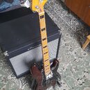 Elektrická basová kytara s tmavě hnědým trupem a hnědým pickguardem. Na hlavě nástroje je nápis Squier PRECISION BASS. Krk má světle hnědou barvu s v…