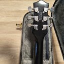 Fotografie zachycuje zadní stranu hlavy černé kytary v otevřeném kufru s šedým polstrováním. Na zadní straně hlavy je bílý nápis CYG21012234 a CRAFTE…