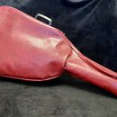 Na fotografii je červený obal na hudební nástroj, pravděpodobně kytaru, vyrobený z materiálu s povrchem imitujícím kůži. Obal má zipové uzavírání a v…