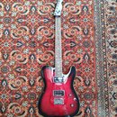 Elektrická kytara s červeným gradientem (sunburst) a viditelnou strukturou dřeva. Nástroj má dva humbuckery, jeden tónový potenciometr a jeden přepín…
