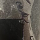 Detailní záběr na povrch hudebního nástroje v šedé metalické barvě. Na lakovaném povrchu jsou viditelné tmavé šmouhy a rýhy připomínající nápisy nebo…