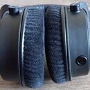 Černá uzavřená sluchátka s velkými polstrováním z černého textilního materiálu. Na pravém sluchátku je viditelný vstup pro jack konektor. Povrch plas…