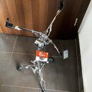 Chromovaný stojan na bicí s třemi rameny zakončenými černými plastovými držáky. Na stojanu je upevněn oranžový a bílý štítek s nápisy „Gintech“ a „G3…