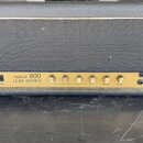Kytarový zesilovač v černém obalu s šedou textilní mřížkou. Zlatý přední panel nese nápis „replica 800 LEAD SERIES“. Na panelu jsou umístěny dva vypí…