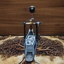 Černý basový pedál s kovovou konstrukcí a stříbrným šlapadlem. Na základně je bílé logo TAMA a pod ním nápis The Legend in Innovation. Pedál vykazuje…
