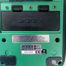 Zadní strana zeleného digitálního záznamového zařízení značky ZOOM. Na černém víčku baterií je vyražen nápis ZOOM a text BATTERY: R6 (SUM-3) or "AA"…