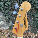 Fotografie zachycuje hlavu elektrické basové kytary z přírodního dřeva. Na povrchu je černý nápis „Westminster ELECTRIC BASS“. Nástroj má čtyři kovov…