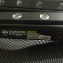 Černý LED panel s řadou kulatých svítidel. Na spodní části je bílé logo ADJ a nápis SWEEPER BEAM QUAD LED s webovou adresou www.adj.com. Vedle se nac…