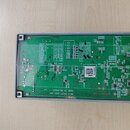 Fotografie znázorňuje zelenou základní desku s elektronickými součástkami v šedém plastovém rámu. Na desce je bílý nápis MAIN SHEET ASSY NAK a MADE I…