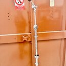 Stříbrný kovový mikrofonní stojan s teleskopickým mechanismem. V horní části je umístěn držák s černým mikrofonem. Povrch stojanu vykazuje drobné zná…