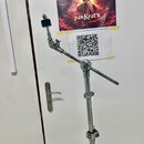 Stříbrný kovový mikrofonní stojan s dvěma kloubovými rameny. Stojan je umístěn před bílou dveřmi, na kterých jsou přilepeny dva papíry. Na horním pap…