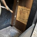 Detail vnitřku kytarového komba s papírovým štítkem přilepeným na dřevěný korpus. Na štítku je text: Model "VIBRO-CHAMP-AMP.AA764", Production #5, Po…