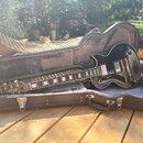 Černá elektrická kytara s tvarem single-cut v tvrdém kufru s šedým polstrováním. Na hlavě hmatníku je bílý nápis Epiphone. Kytara má dva humbuckery,…