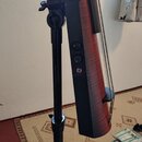 Detailní pohled na spodní část těla elektrického kontrabasu v černé a červeně dřevěné barvě, který stojí na černém stojanu. Na černé části těla jsou…