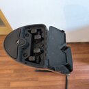 Černý plastový držák na nástroj s otevřeným víkem. Uvnitř jsou vidět čtyři šrouby a dvěstřanný mechanismus pro uchycení. Na horní části je vyryto tro…