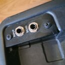 Detailní pohled na černý plastový panel s dvěma kovovými konektory. Vedle levého konektoru je bílý nápis INPUT a vedle pravého nápis SEND. Panel je p…