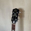 Černá hlava elektrické kytary s chromovanými ladičkami. V horní části je bílé logo "fender" a pod ním nápisy "Custom Shop" a "Made for Czech Republic…