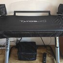 Černý krycí plášť přes klavír nebo syntezátor s nápisem Tyros 4. Nástroj stojí na stříbrném stojanu, na kterém jsou viditelné nápisy YAMAHA a SHURE.…