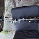Fotografie zobrazuje chromovaný basový pedál položený na černém podkladu. Nástroj je vyroben z kovu s černými plastovými či gumovými prvky na pedálec…