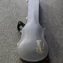 Černý tvrdý kufřík na kytaru s nosním popruhem. Na spodní části je zlatým písmem nápis Gibson Custom. Povrch kufříku vykazuje mírné známky opotřebení…