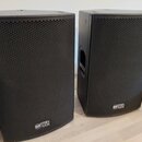 Dva černé reproduktory s kovovými mřížkami a zaobleným spodním okrajem. Na spodní části obou reproduktorů je umístěn štítek s nápisem RCF TT 02. Povr…