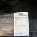 Fotografie zobrazuje dvě papírové karty v černé obálce. Levá karta nese nadpis LIMITED WARRANTY a text v angličtině od výrobce Ernie Ball Music Man.…