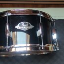 Černý buben s chromovaným obručováním a napínacími šrouby. Na korpusu je viditelný štít s nápisy Pearl a EXPORT SERIES DRUMS. Povrch nástroje je glos…