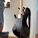 Zadní strana elektrické kytary s černým lesklým povrchem a světle hnědým krkem. Na zadní straně těla je vidět stříbrný kovový kryt krkovnice a černý…