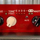Detail ovládacího panelu červeného zesilovače. Na panelu jsou čtyři otočné knofíky a nápisy MIDDLE, TREBLE, TONE® PRINT, MASTER a MUTE. V horní části…