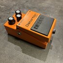 Oranžový efekt pedál s černým spínacím tlačítkem. Na horní části je nápis Distortion a označení DS-1, na tlačítku je logo BOSS. Pedál má tři černé ov…
