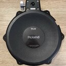 Černý kruhový trigger pad z gumového materiálu s plastovým rámem. Uprostřed je bílý nápis Roland a nad ním štítek s označením PDX-100 DUAL TRIGGER PA…