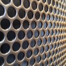 Detailní záběr na kovovou ochrannou mřížku mikrofonu. Mřížka je tvořena pravidelnou strukturou kulatých otvorů v tmavě šedé nebo černé barvě. Povrch…