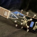 Detail hlavy a části hmatníku elektrické kytary v tmavě hnědé barvě. Na hlavě je bílé logo "Echo", zlatý ornament a modrý štítek s nápisy "Musikalien…