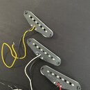 Tři elektrické snímače typu single-coil s černým plastovým krytem a bílými magnety. Na spodní straně dvou snímačů je čitelný nápis 016730, u horního…