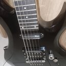 Černá elektrická kytara s tmavým hmatníkem a bílými polohovými značkami. Nástroj má jeden snímač typu humbucker v pozici kobylky a jeden jednoduchý s…