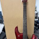 Elektrokytara s červeným kovovými lakem a hnedým hnedým hmatníkem. Na hlavě nástroje je svisle napsaný bílý nápis MUSICMAN. Tělo kytary má v dolní čá…
