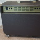 Zadní strana černého akustického kytarového komba s texturovaným povrchem a kovovými rohy. Na horním panelu je nápis ACOUSTIC GUITAR AMPLIFIER a ozna…